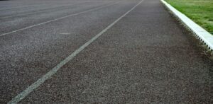 Detailed view of an empty athletic running track lane with visible surface texture and grass edge.